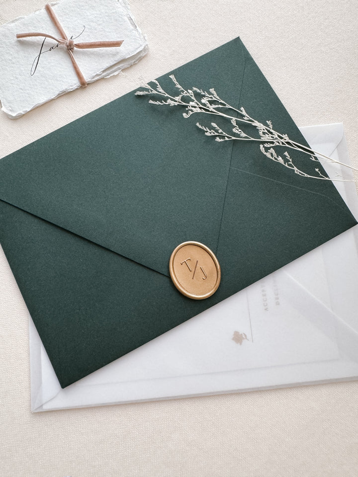 Gold oval monogram wax seal on a dark green envelope