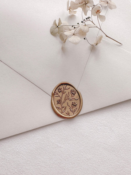 Oval floral gold wax seal with 3D engraving details on a beige envelope styled with a beige flower branch