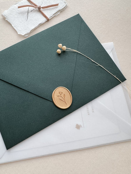 Light gold oval simple floral wax seal on a dark green envelope