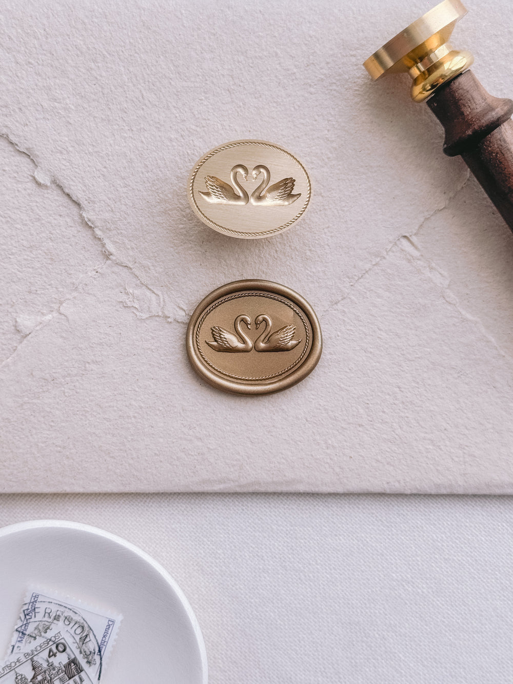 Oval double swans gold wax seal on a beige handmade paper envelope with a brass wax stamp head and wax stamp with a wooden handle