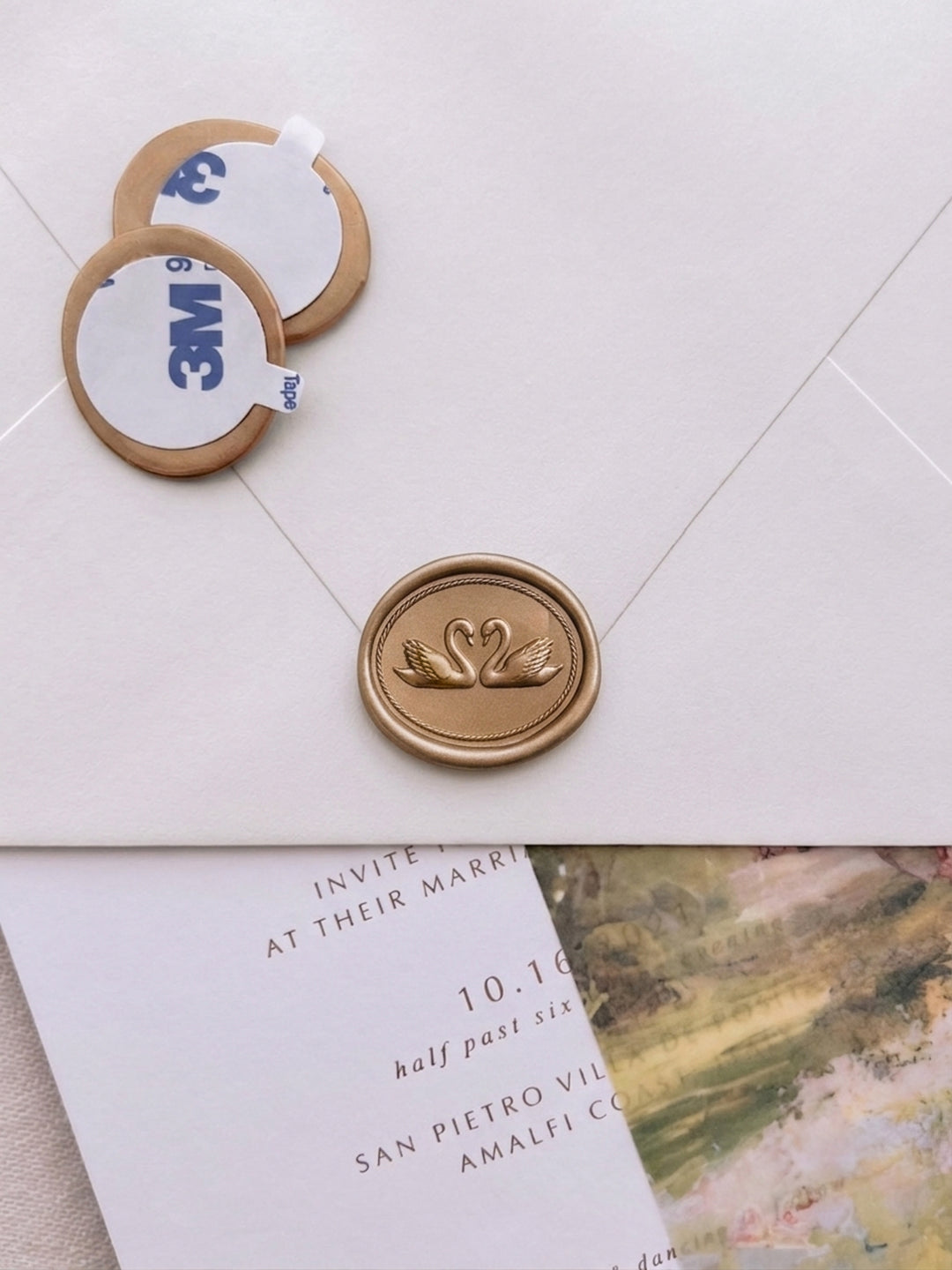 Gold double swan wax seal stickers with adhesive backing displayed beside a sealed ivory wedding envelope and watercolor wedding vellum jacket and invitation card