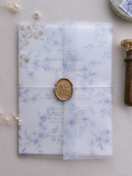 gold vintage monogram wax seal featuring interlocked initials on a blue floral print wedding invitation vellum jacket