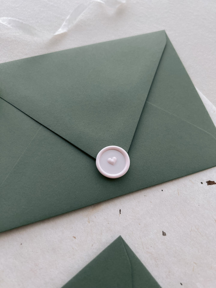 Light pink mini heart wax seal on an olive green envelope 