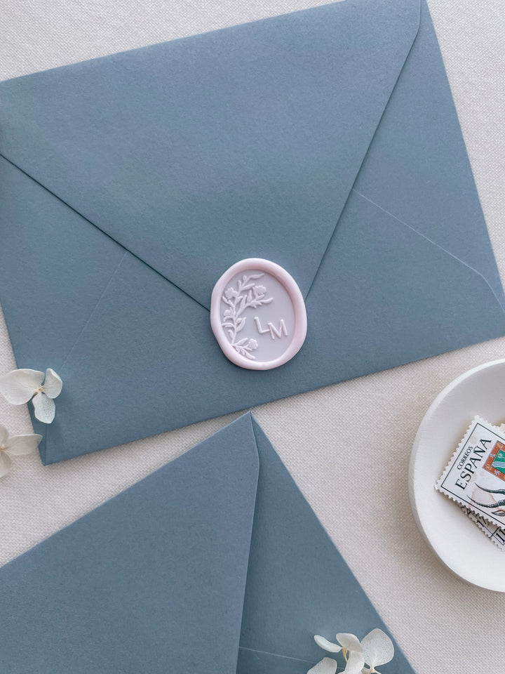 Soft pink custom monogram oval wax seal with personalized initials on a dusty blue envelope