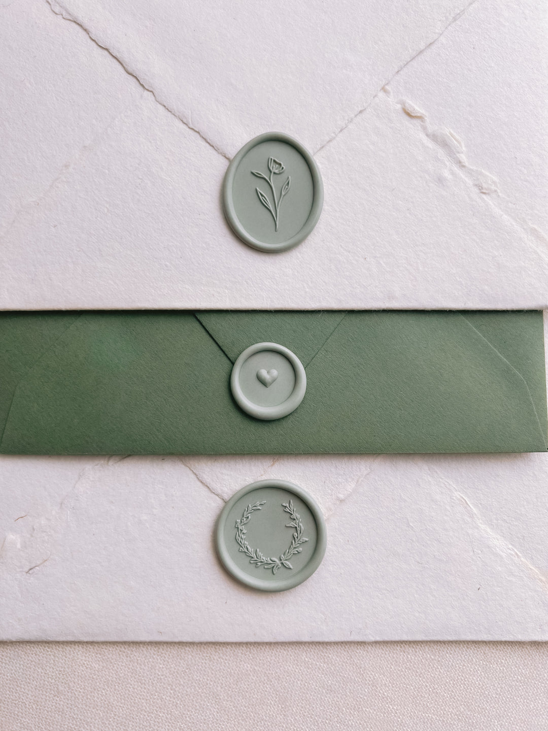 Light sage green colored wax seals featuring a flower design, a mini heart design and a delicate wreath design 