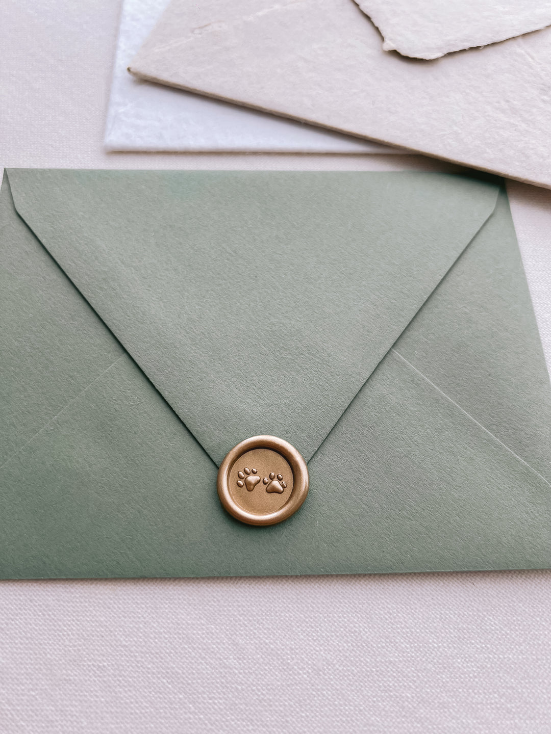 gold paw print mini wax seal with 3D engraving on an olive green envelope 