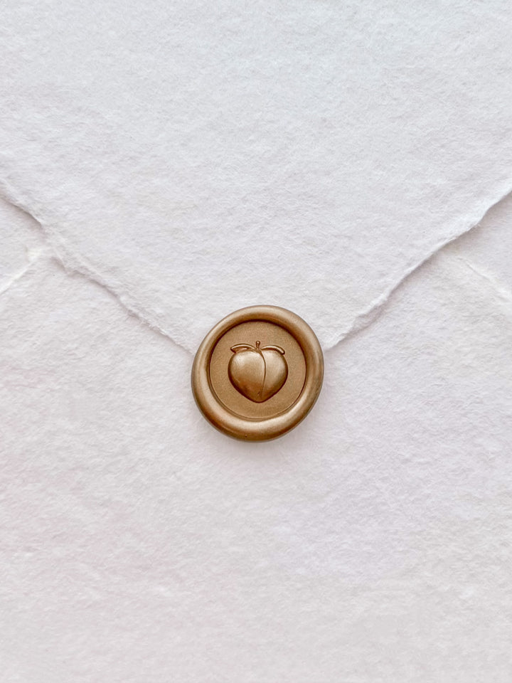 Gold 3D peach mini wax seal on a white handmade paper envelope 