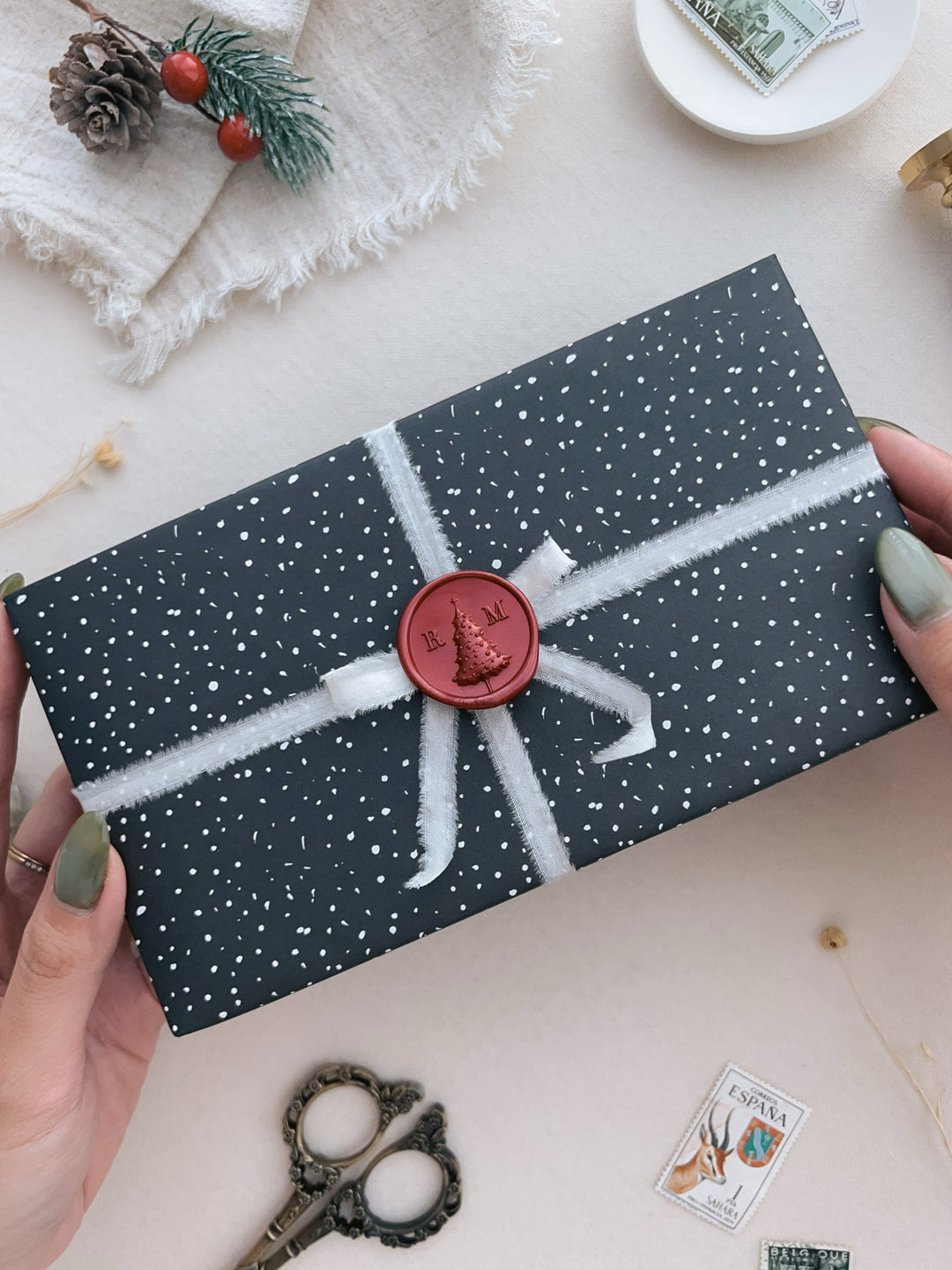 Dark metallic red custom Christmas tree monogram wax seal with personalized initials, decorated on a wrapped gift and silk ribbon
