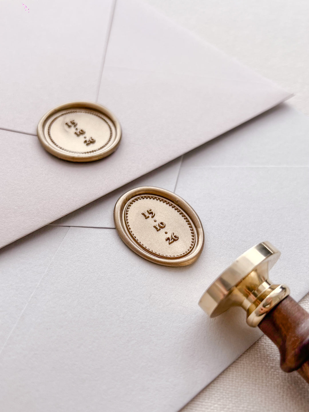 Gold personalized wax seals featuring custom wedding dates on light grey envelopes with a wax stamp head and a wooden handle