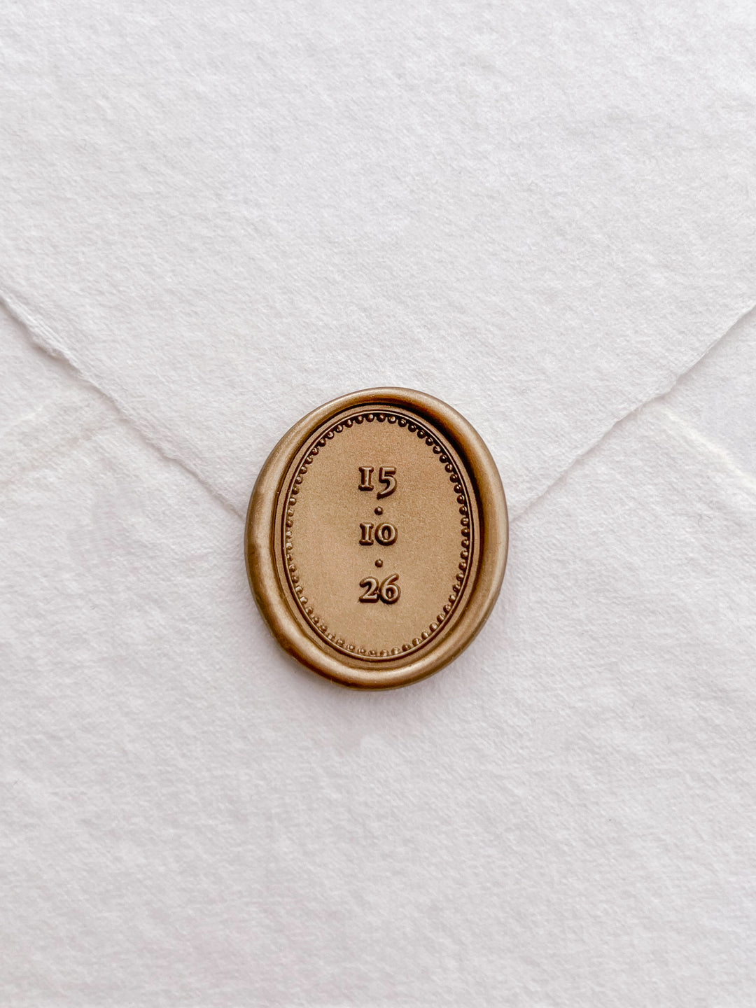 Personalized date oval gold wax seal featuring a custom wedding date on a white deckled edge handmade paper envelope 