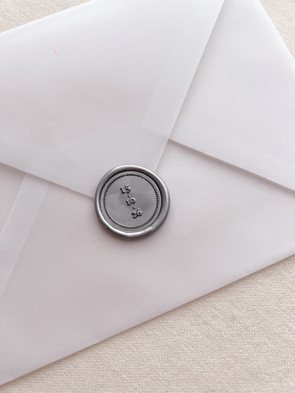 Personalized silver wax seal featuring a custom date on a vellum envelope on a light beige background 