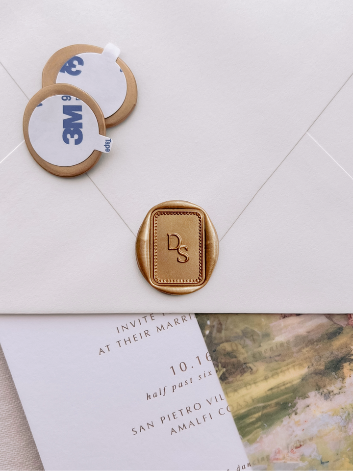 rectangular classique border monogram gold wax seal stickers with self-adhesive backings on a wedding invitation, beige envelope, and floral vellum jacket
