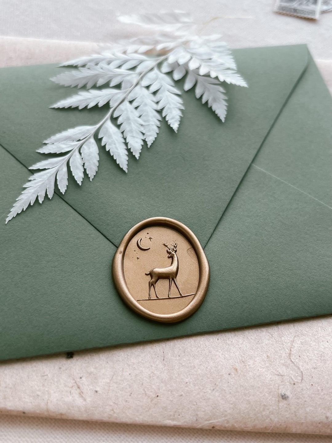 Gold 3D reindeer oval wax seal on an olive green envelope 