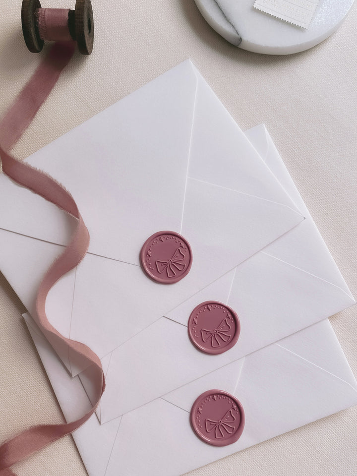 Ribbon bow wax seals in rosewood color on white paper envelopes styled with a strand of rose silk ribbon