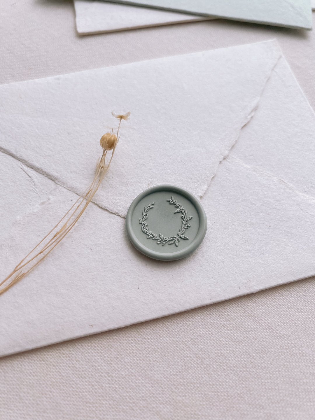 Sage green colored botanical wreath design wax seal on a white envelope