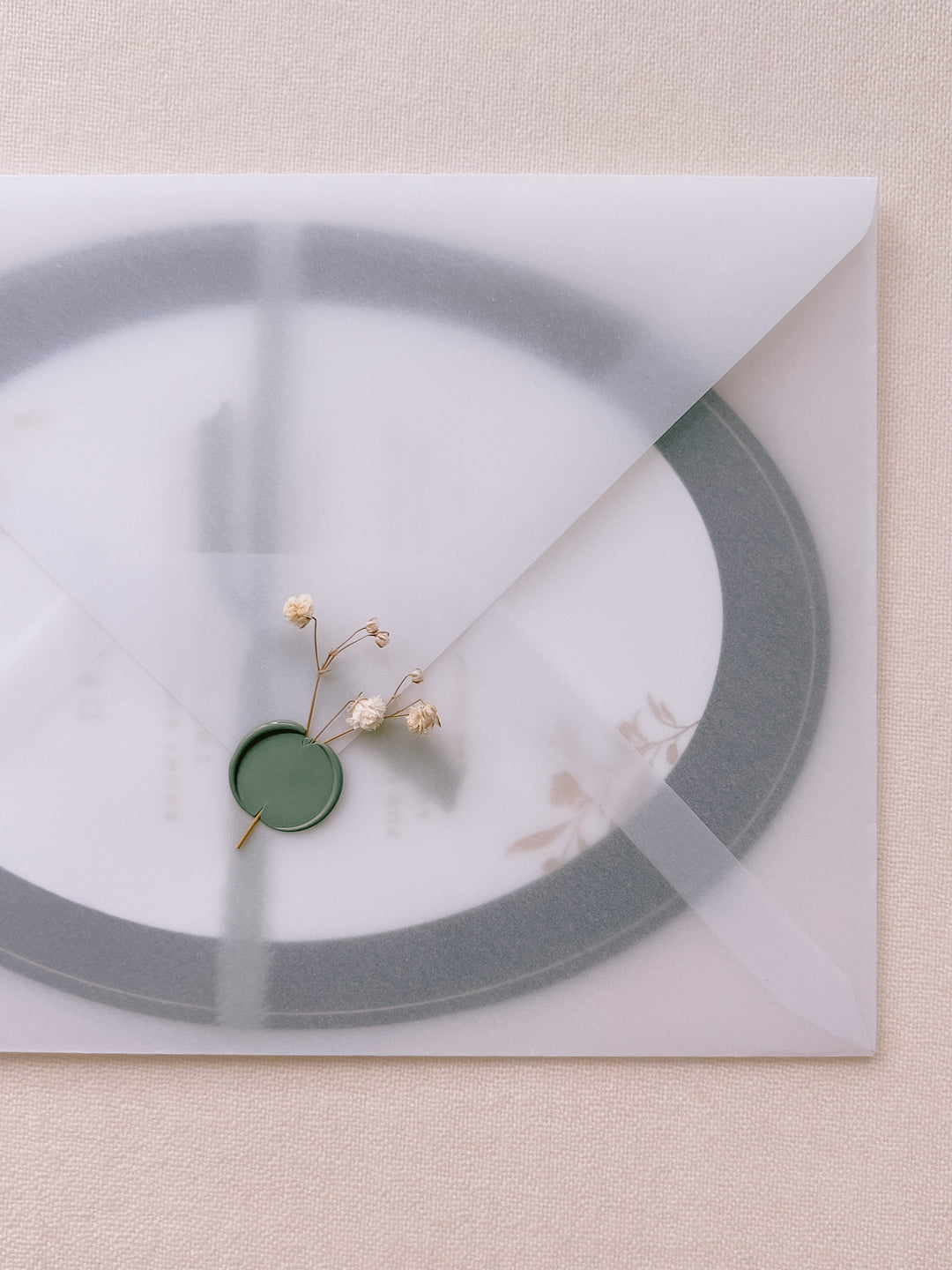 blank wax seal in sage green embellished with white dried flowers on vellum envelope