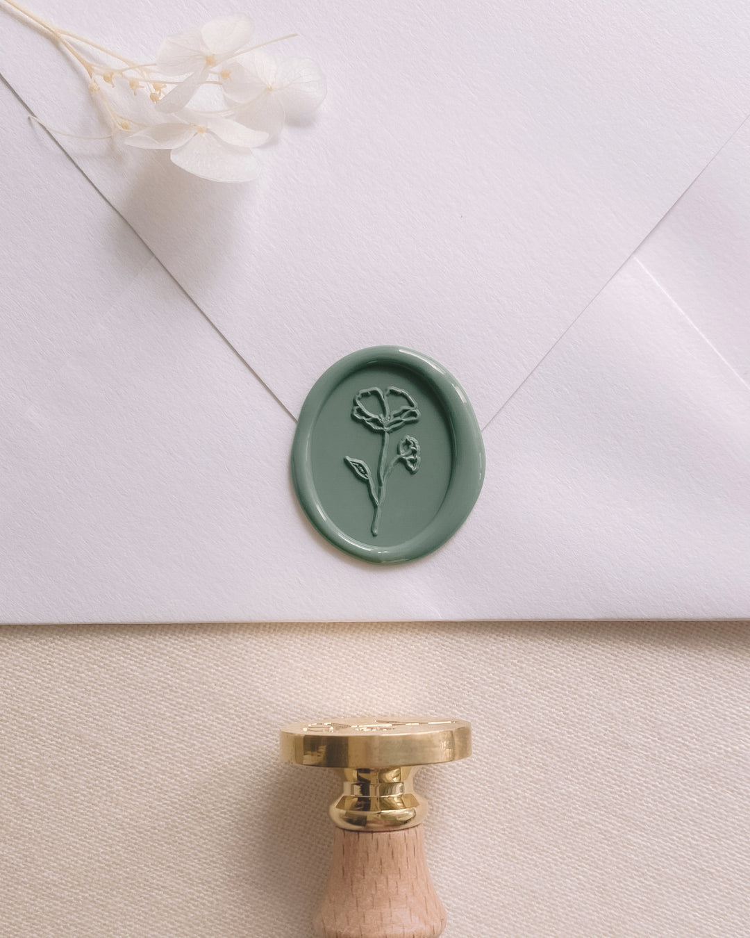 Oval flower wax seal in sage green on white envelope