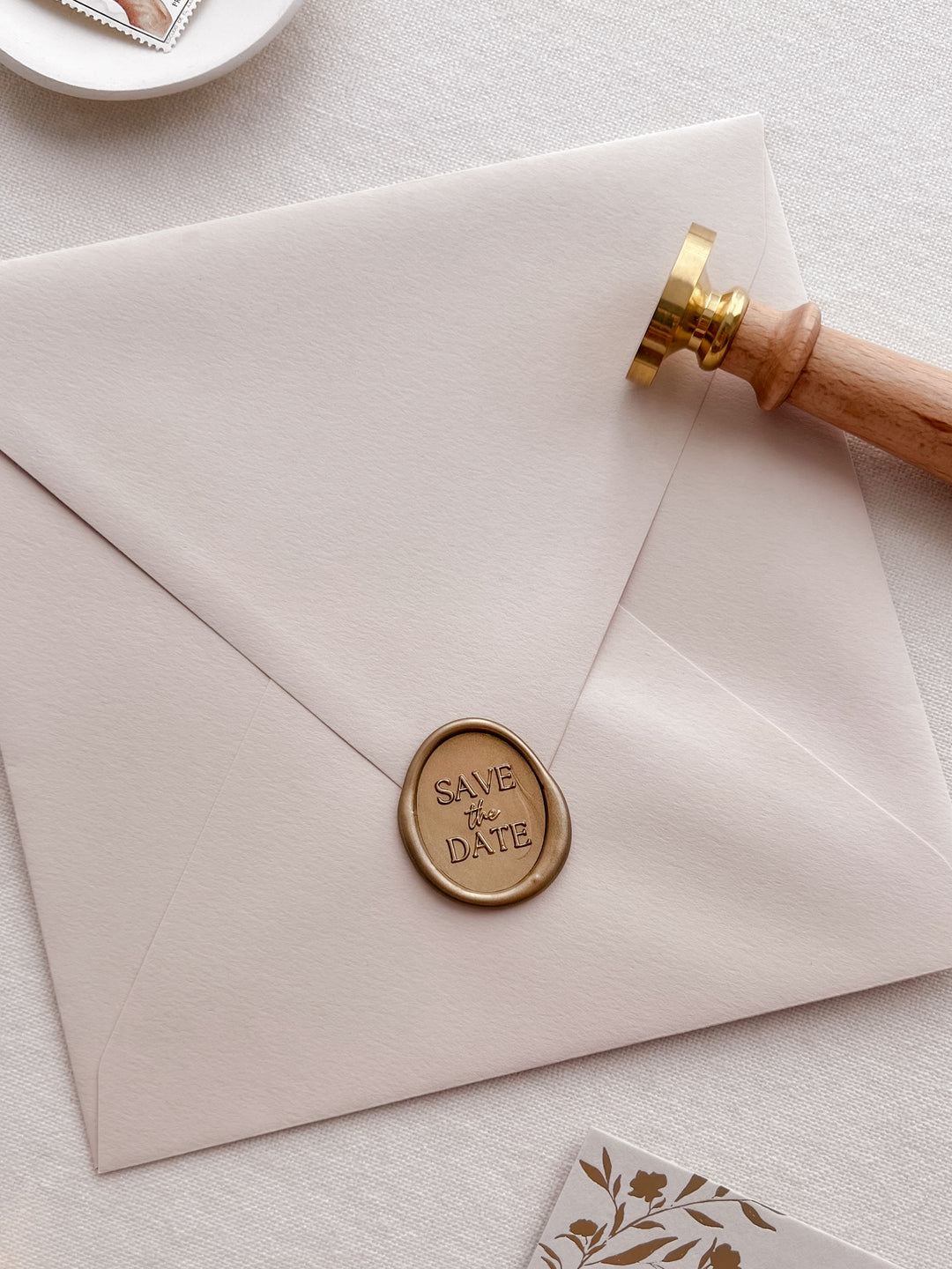 Gold save the date oval wax seal on a beige envelope 