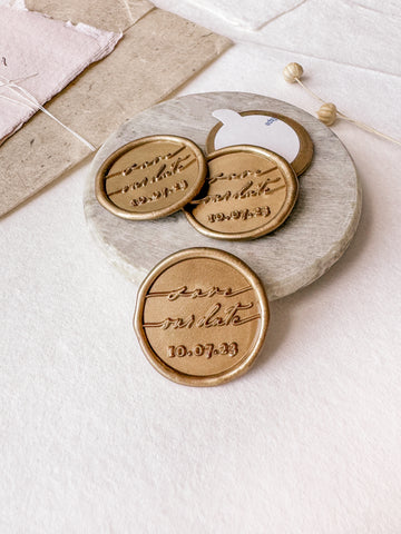 Personalized save our date custom wax seals in gold styled with a small gray stone dish, handmade paper and a dried floral branch