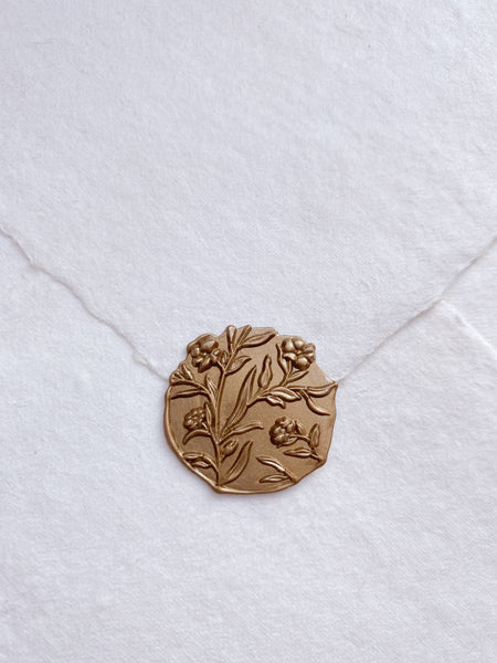 Gold edgeless flower wax seal on a white handmade paper envelope