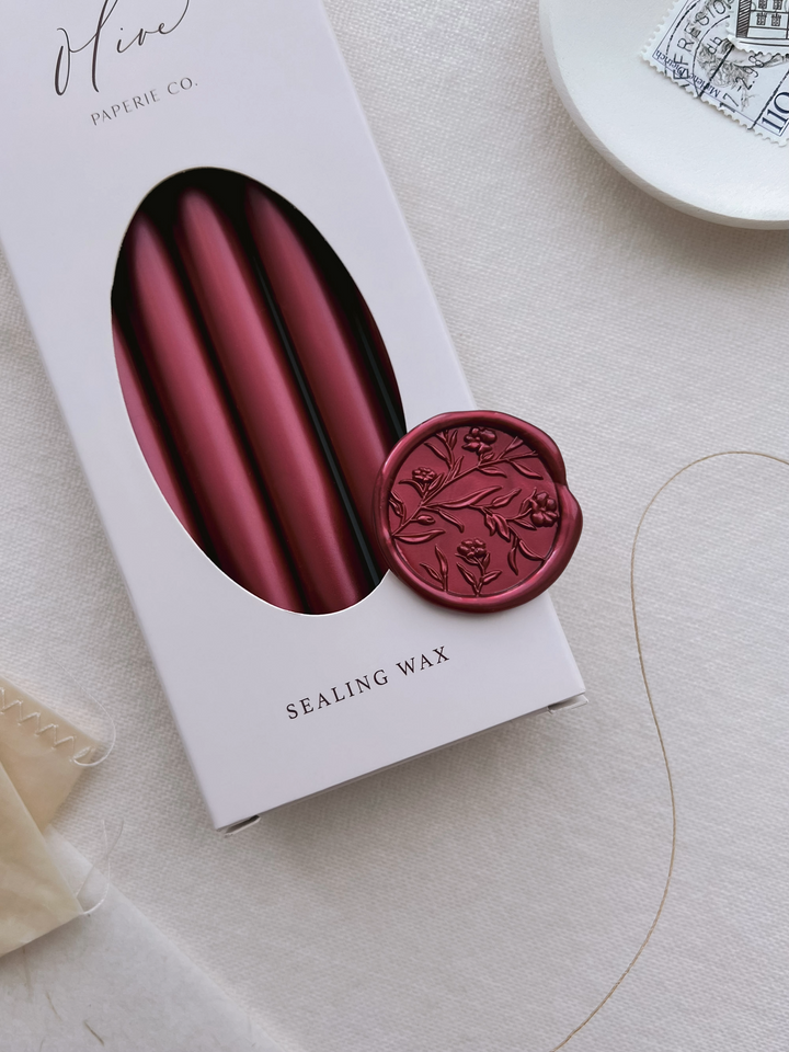 Dark metallic red floral wax seal on a box of metallic red sealing wax sticks