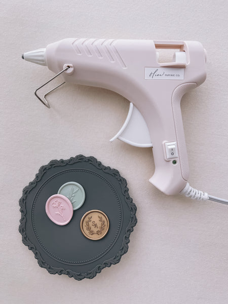 beige low heat glue gun for wax seal making, next to a gray silicone mat and wax seals 