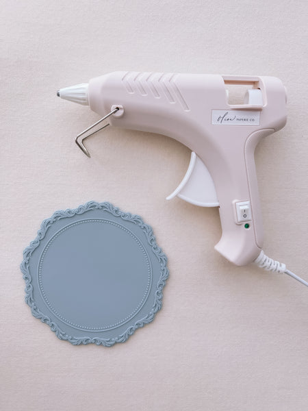 beige low temperature glue gun for wax seal making, next to a light blue silicone mat