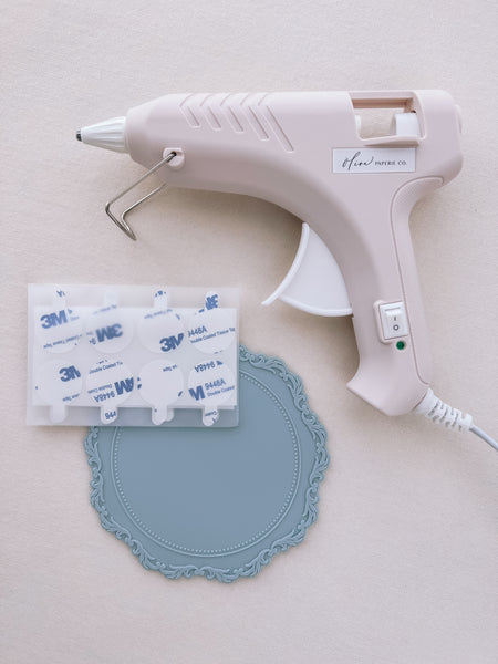 beige low heat glue gun for wax seal making, next to a light blue silicone mat and 3M adhesive backing stickers