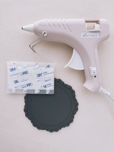 beige low heat glue gun for wax seal making, next to a gray silicone mat and 3M adhesive backing stickers