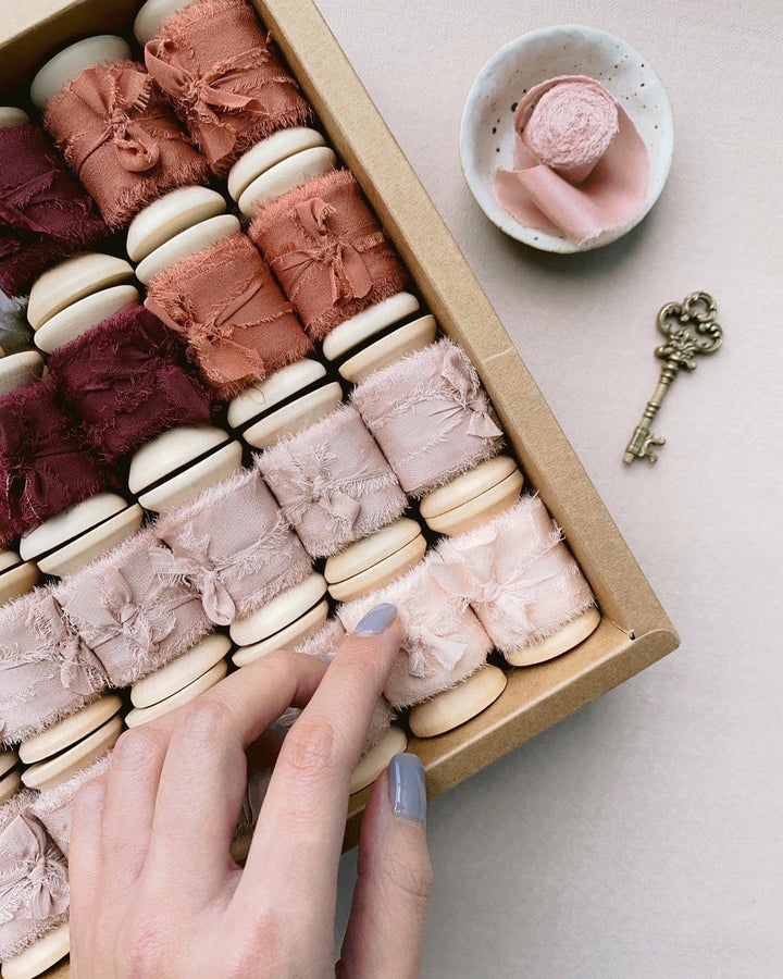 A box of raw edge silk ribbons on wooden spools in color Nude, Pale Mauve, Clay and Wine