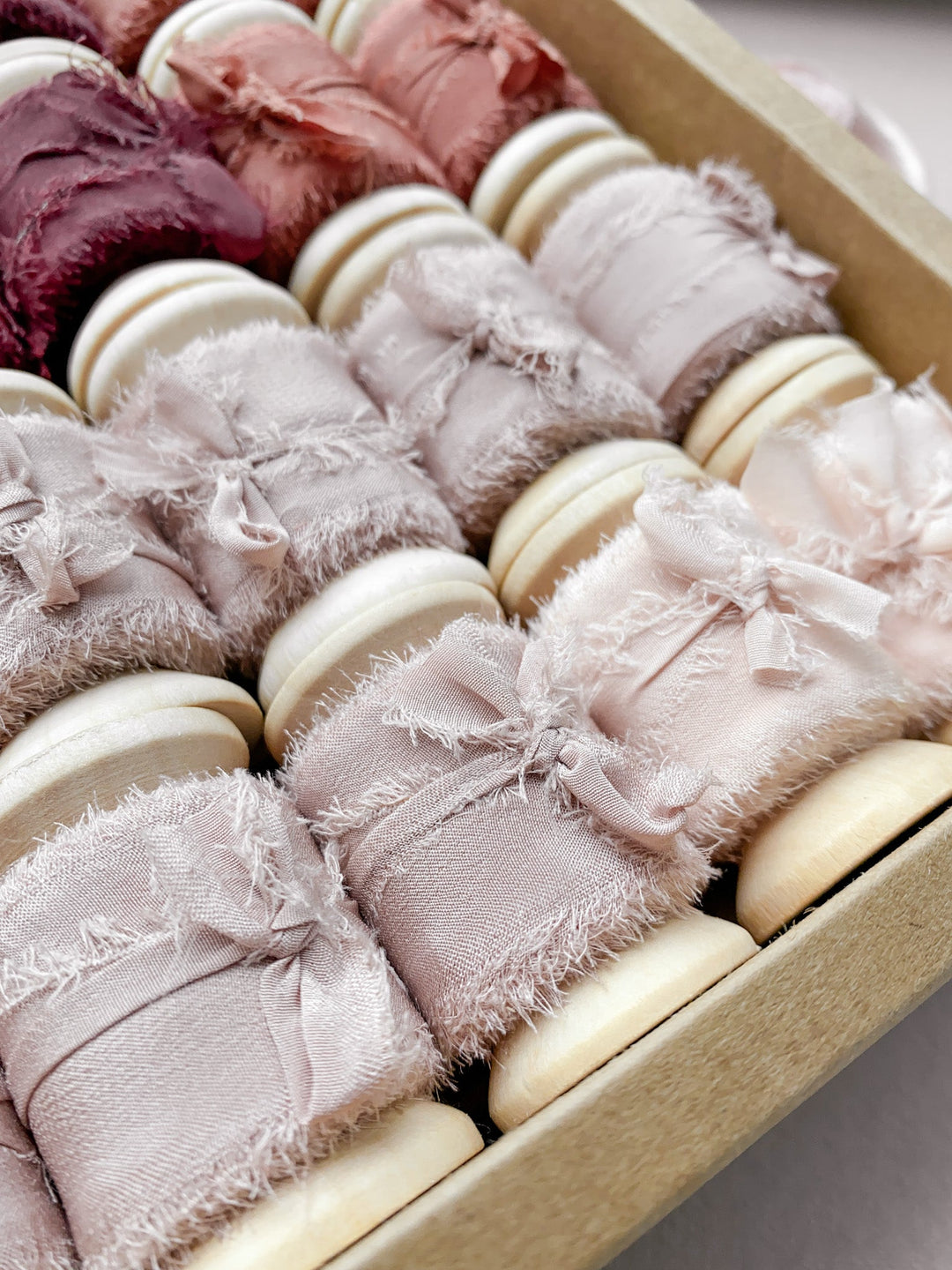 A box of raw edge silk ribbons on wooden spools in color Nude, Pale Mauve, Clay and Wine  Edit alt text