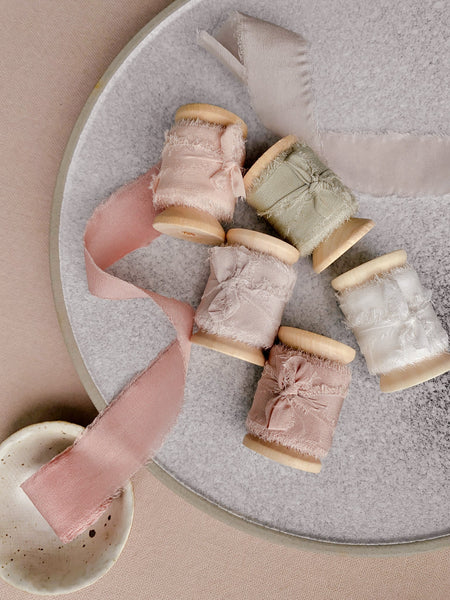 1 inch raw edge silk ribbon on wooden spools in color Soft White, Nude Grey, Nude, Sage, Pale Mauve, and Blush