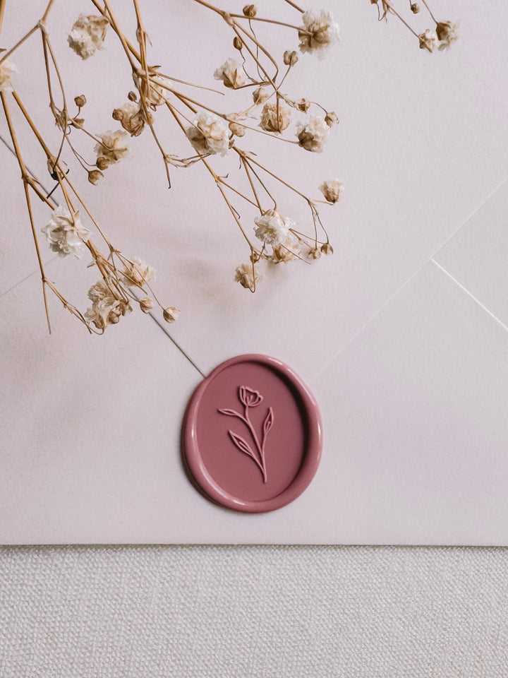 Dusty rose oval floral wax seal on a light beige envelope styled with dried floral branches