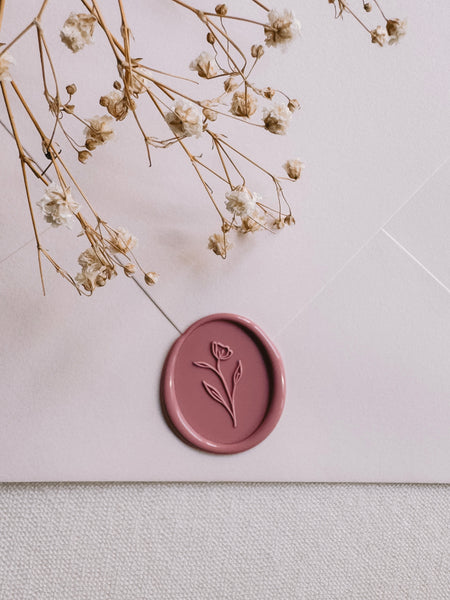 Dusty rose oval floral wax seal on a light beige envelope styled with dried floral branches