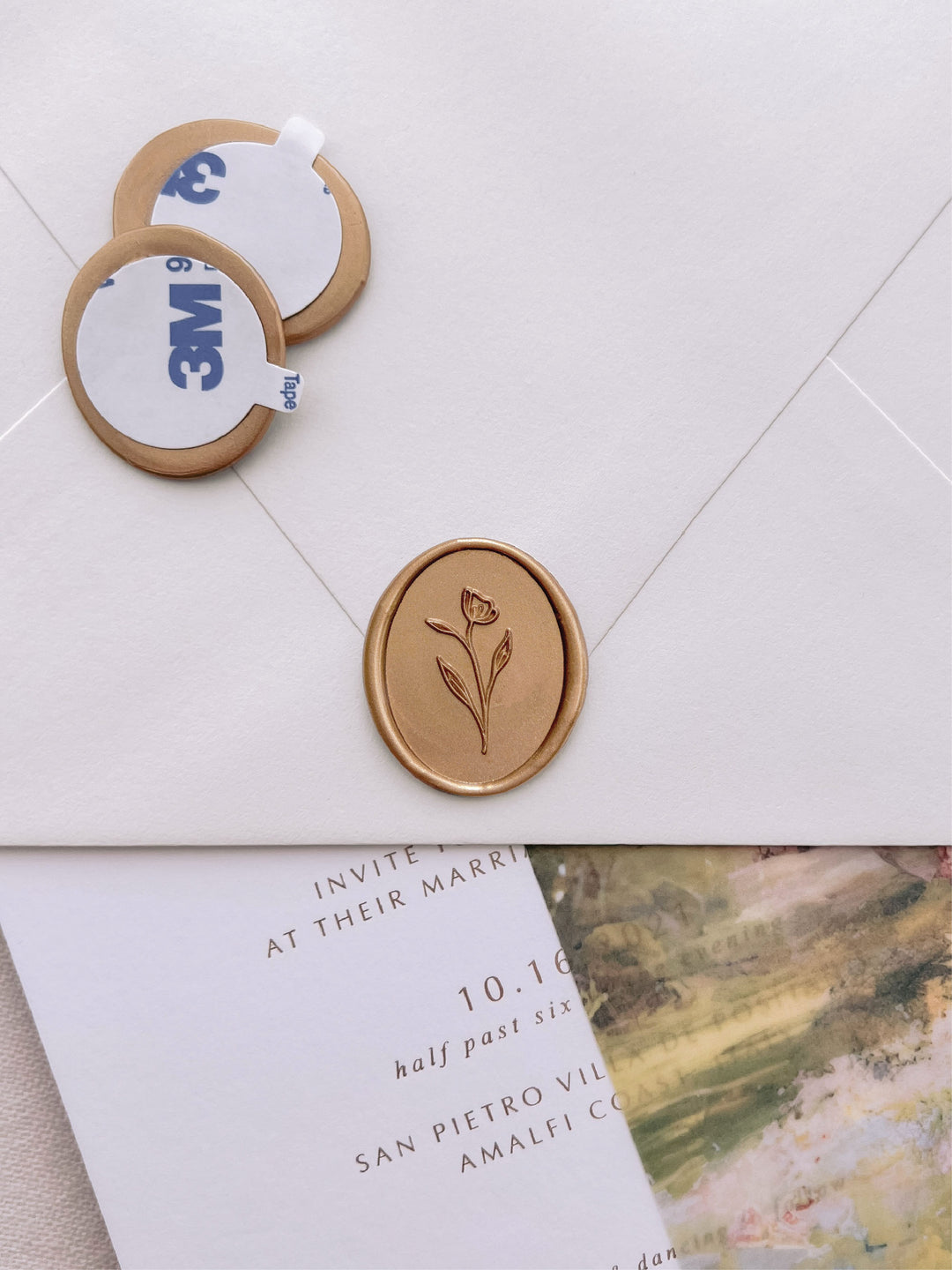 simple floral oval gold wax seal stickers with self-adhesive backings on a wedding invitation, beige envelope, and floral vellum jacket
