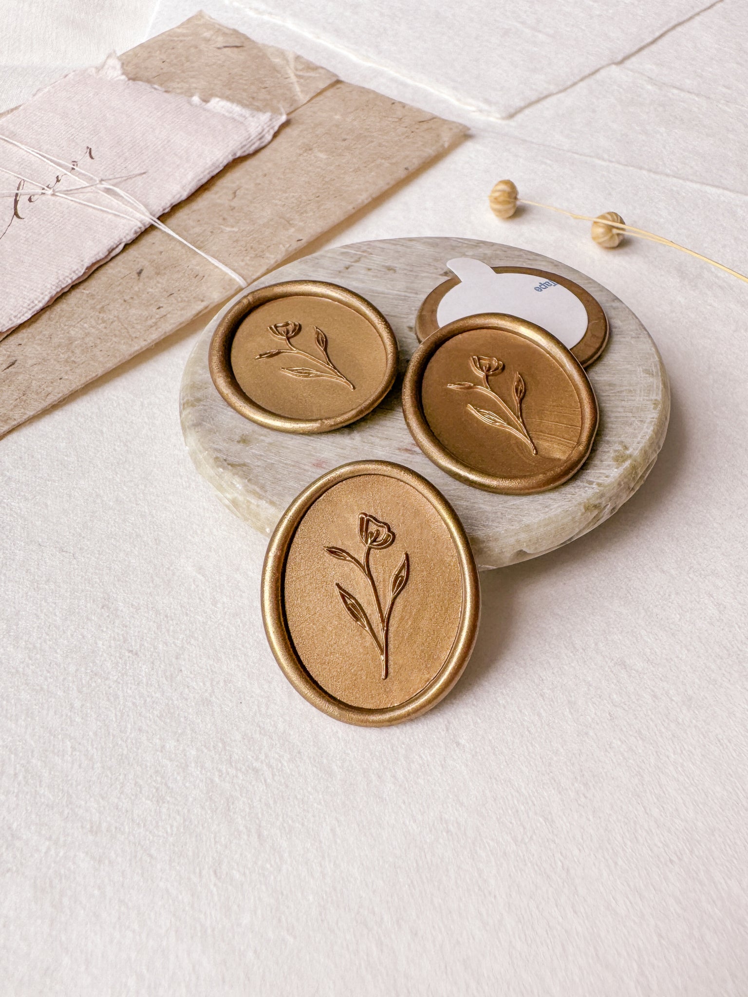 Simple flower oval wax seals in gold styled with a small gray stone dish, handmade paper and a dried floral branch