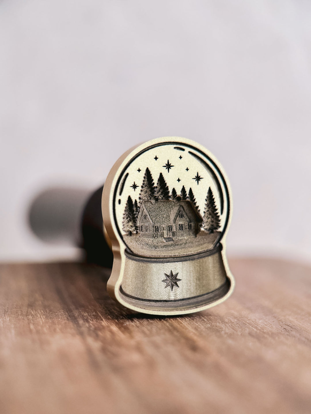Die-cut brass snow globe wax seal stamp with north star detail, standing upright on a wooden surface with the wooden handle behind.