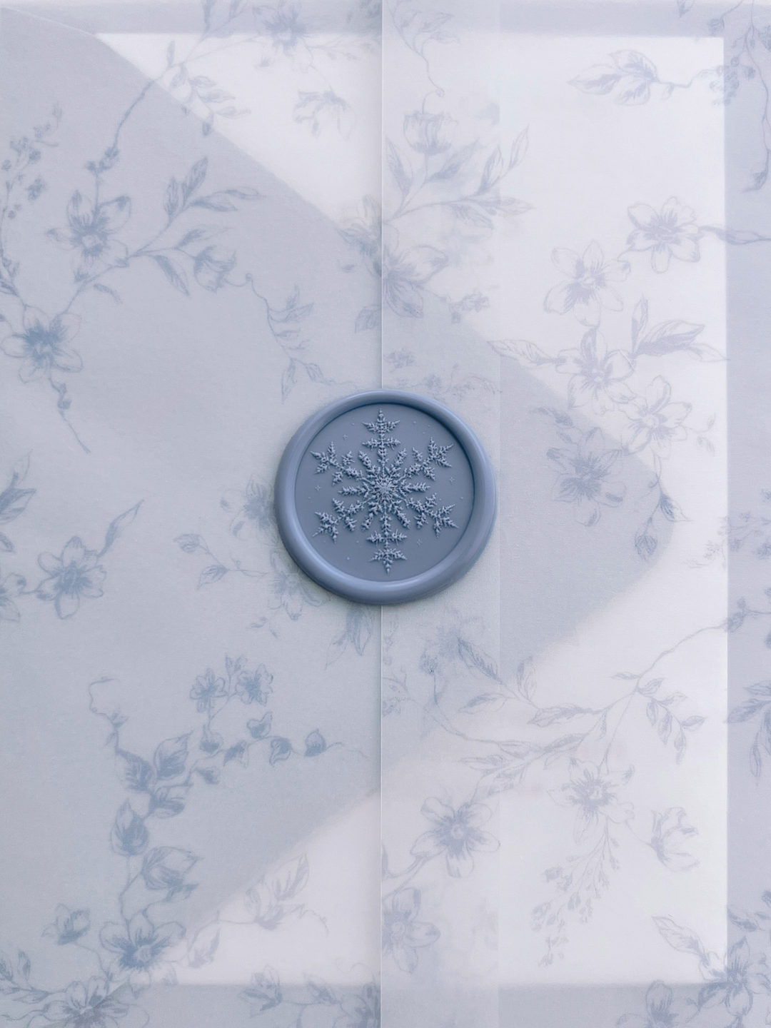 Dusty blue snowflake wax seal with 3D engraving on a translucent blue floral print vellum jacket