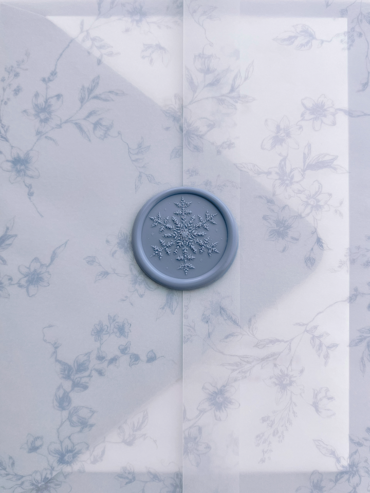 Dusty blue snowflake wax seal with 3D engraving on a translucent blue floral print vellum jacket