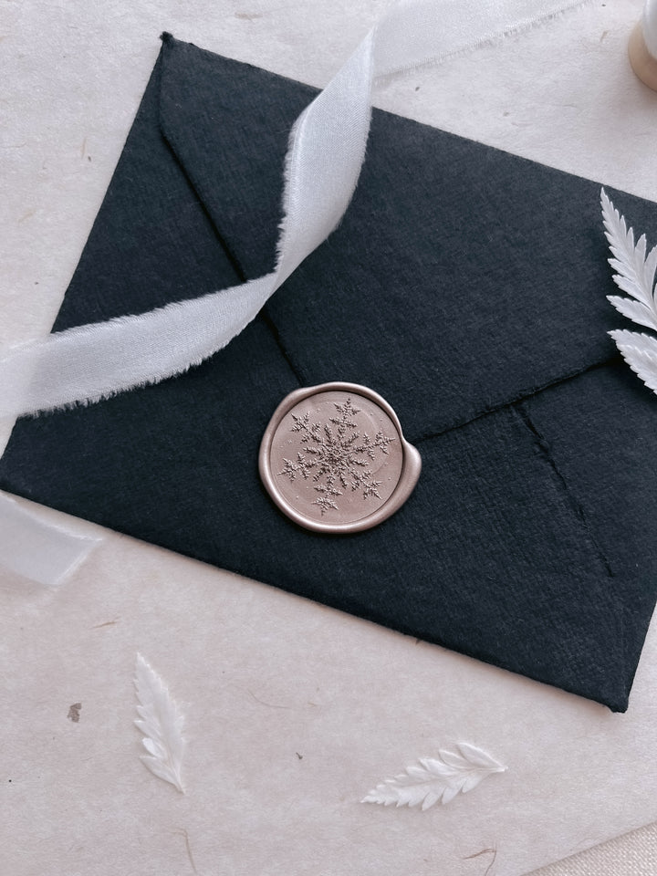 Light bronze snowflake wax seal on a black deckle edge handmade paper envelope