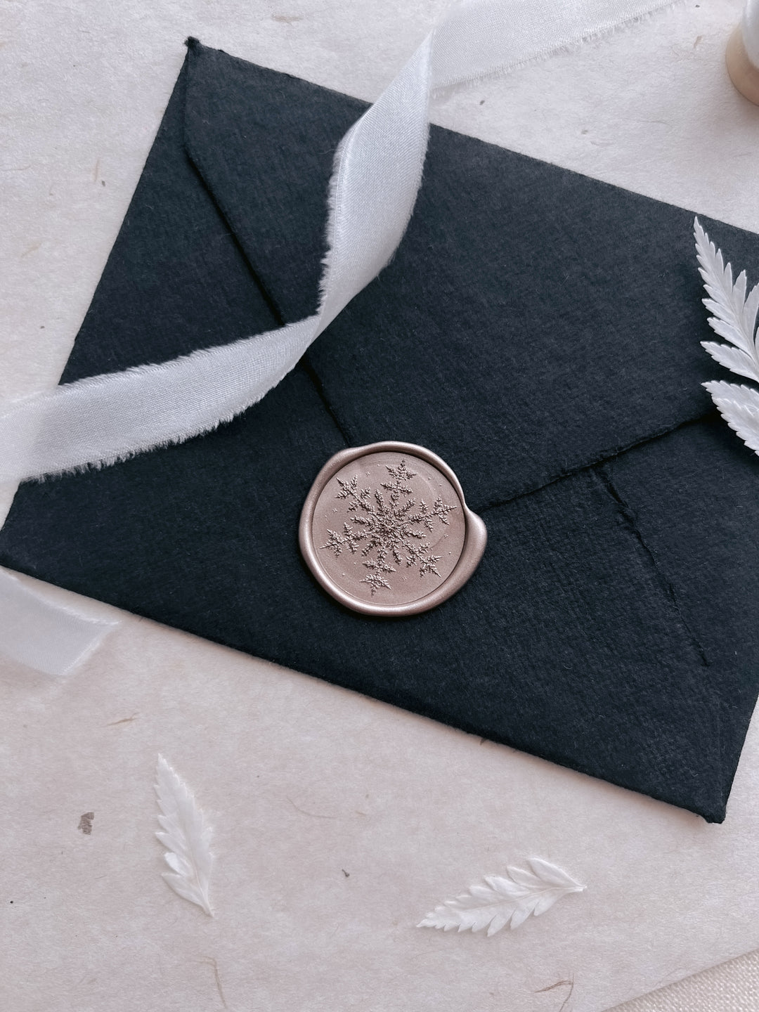 metallic champagne colored snowflake design wax seal on a black envelope