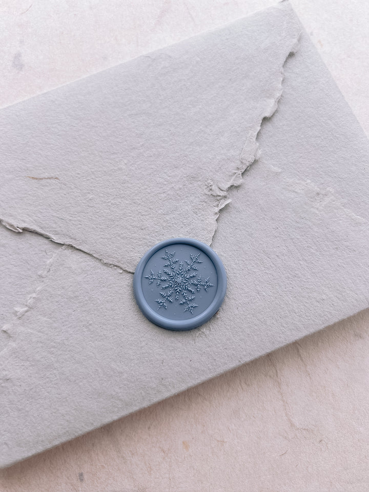 Dusty blue 3D engraved snowflake wax seal on a light grey deckled edge handmade paper envelope 