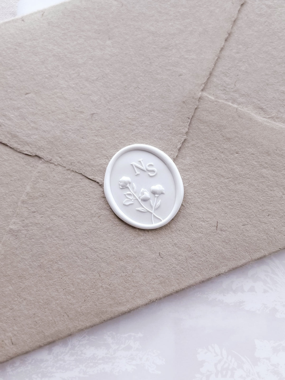 White custom monogram floral design oval wax seal on a beige envelope 