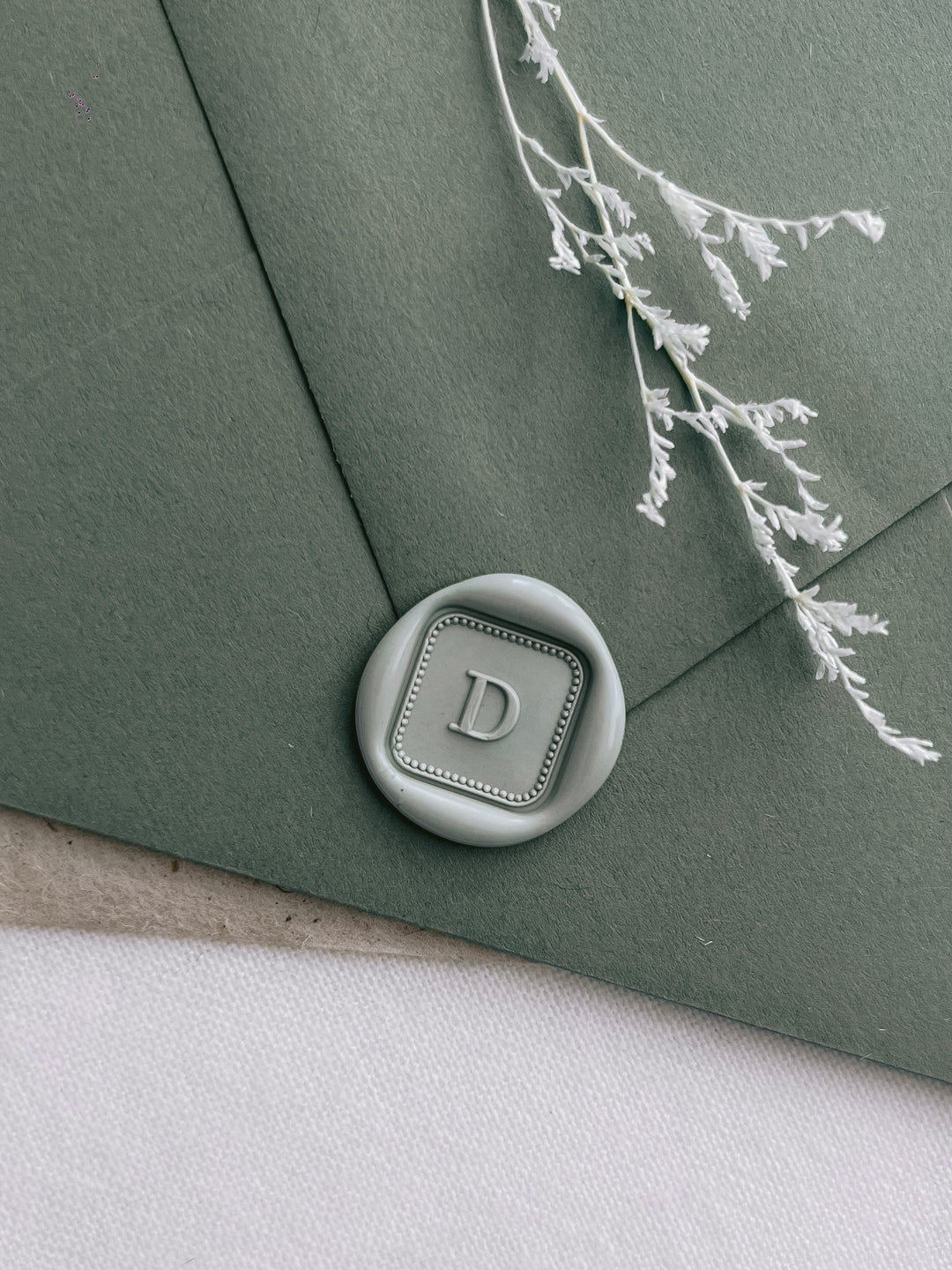 sage green custom initial square wax seal on olive green envelope