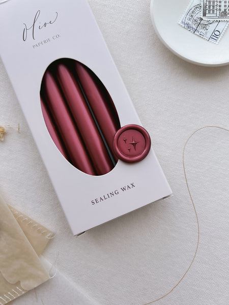 Dark metallic red star emoji wax seal on a box of metallic red sealing wax sticks
