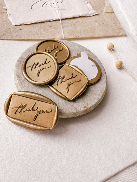Calligraphy script "thank you" wax seals in gold with 3M stickers on small gray stone dish