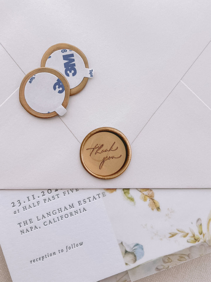 thank you gold wax seal stickers with self-adhesive backings on a wedding invitation, beige envelope, and floral vellum jacket