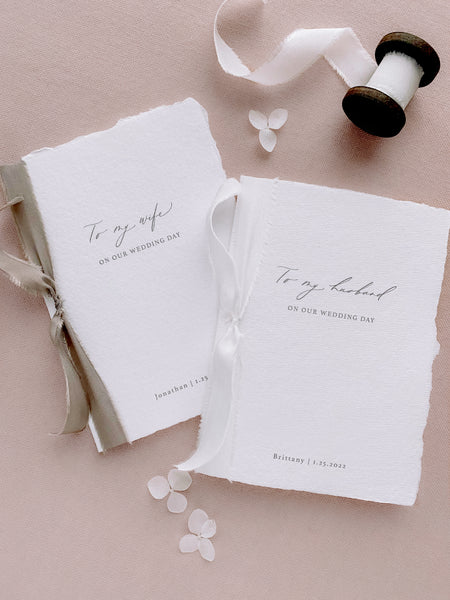 A set of two His and Her personalised wedding love letters handmade paper vow books in modern calligraphy script with one tied in soft white colored silk ribbon and the other tied with sage colored silk ribbon styled with spool of soft white silk ribbon