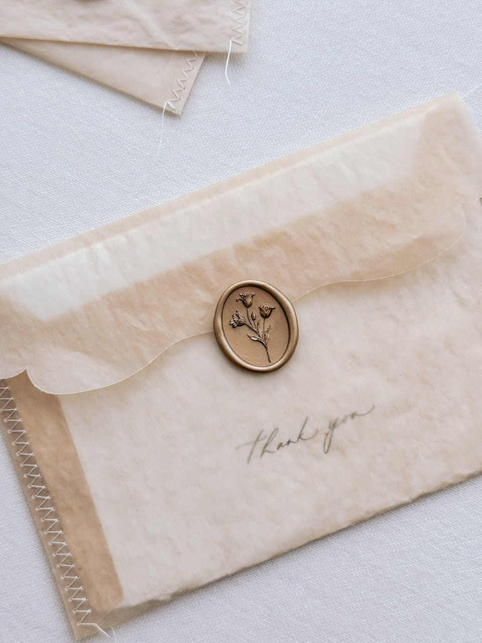 Gold tulip wax seal on a brown vellum envelope with handwritten "thank you" note inside