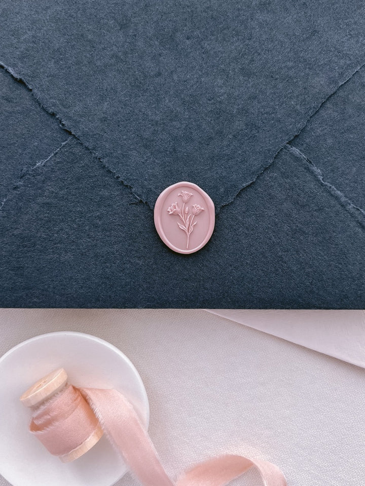 Blush pink tulip wax seal on a black deckle-edge wedding invitation envelope, paired with blush silk ribbon.